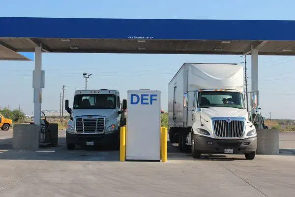 Two trucks under a blue canopy with a DEF island between them.