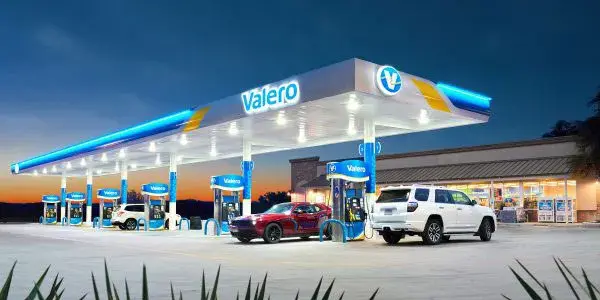 Glowing Valero site at dusk, with a red and a white car at the pumps.